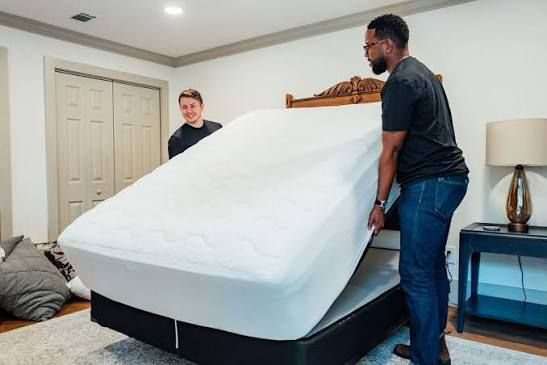 Two crew members lifting a mattress off a bed frame
