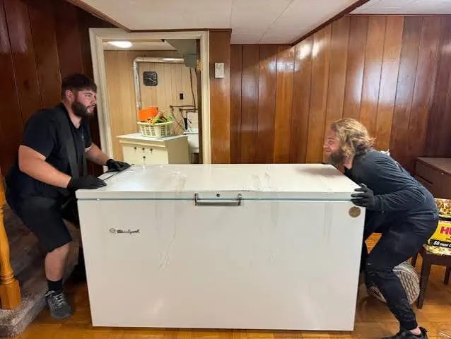 Two workers moving a chest freezer out of a room